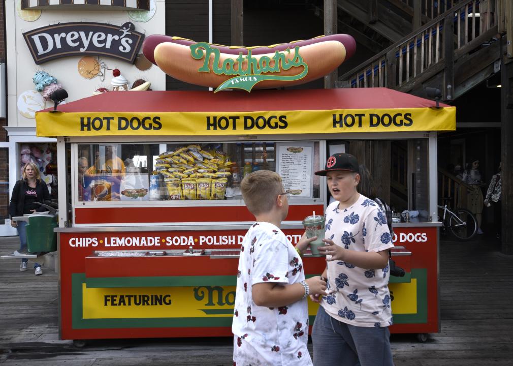Two boys talk next to a hot dog vendor.